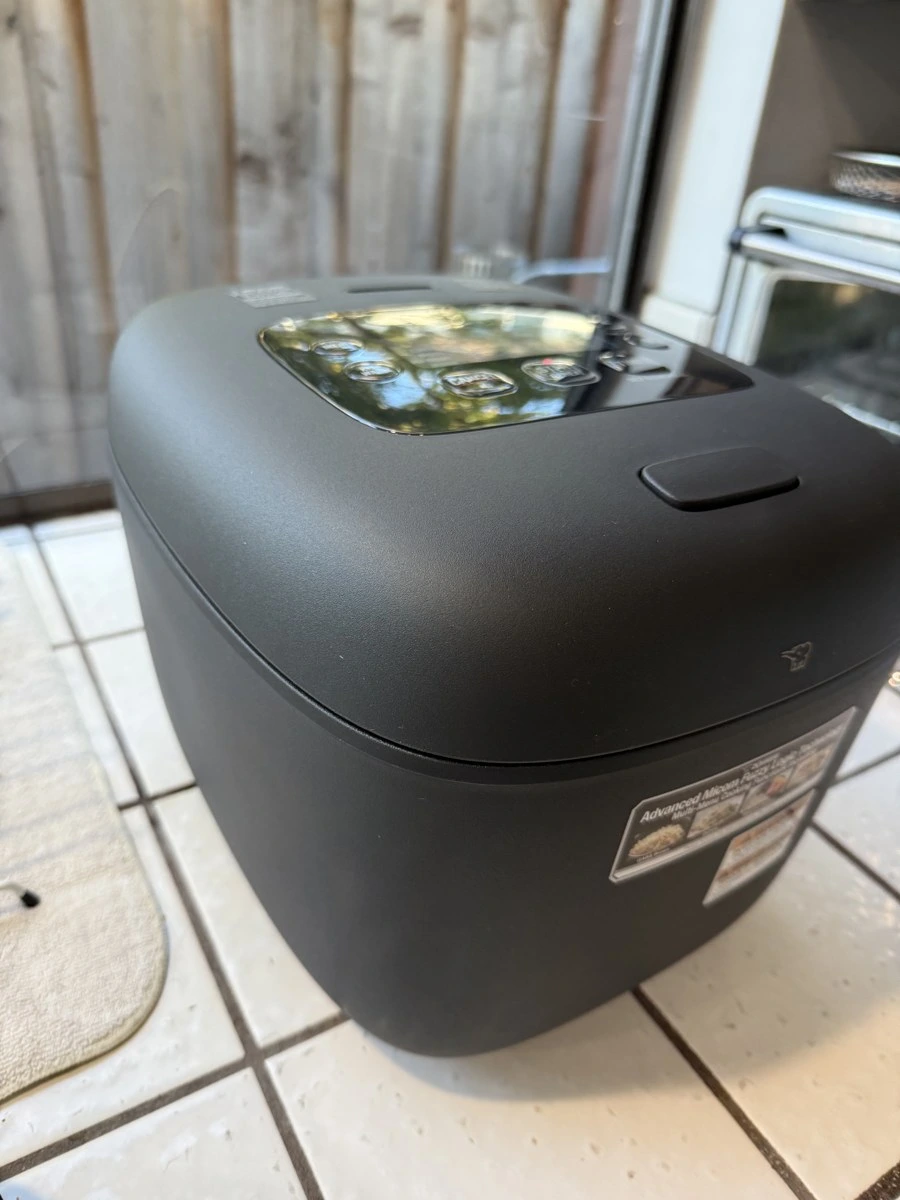 Matte-black Zojirushi NL-EAC18BA 10-cup Micom rice cooker on my kitchen counter showing the flat top panel, lid-release button, and elephant logo